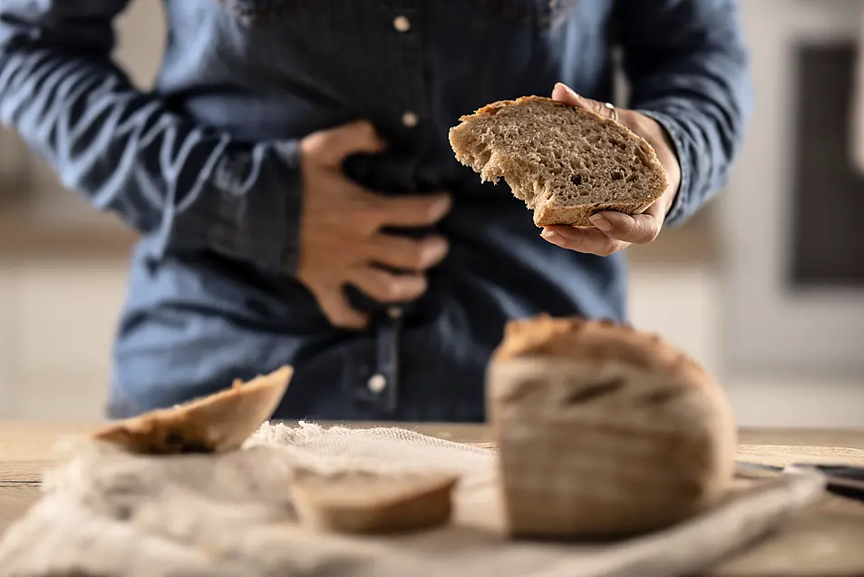 Woman experiencing stomach pains after eating a slice of brown bread