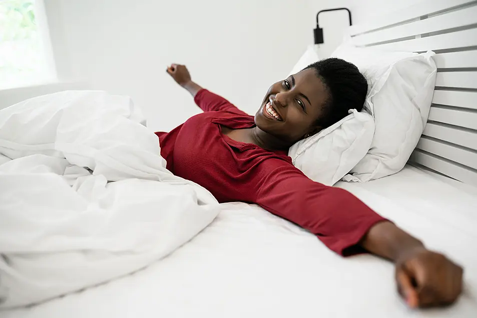 A woman lying in bed in the morning with outstretched arms and smiling 