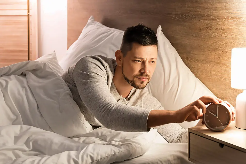 Man setting an alarm while lying in bed at night