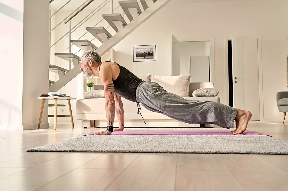 Mature man doing a plank on yoga mat at home 