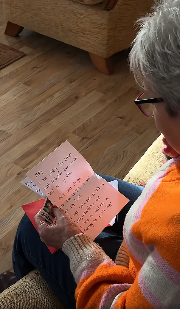 An elderly woman sat on her sofa and looking down at a handwritten letter