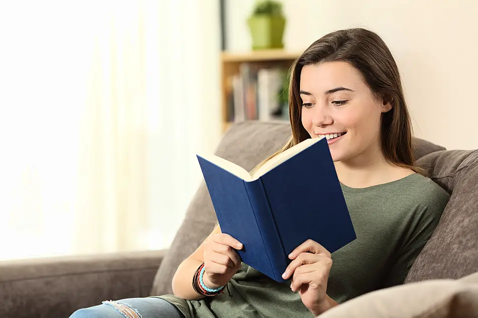 A woman sat on a sofa reading a book