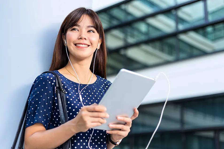 Happy young woman holding an iPad and listening to a podcast