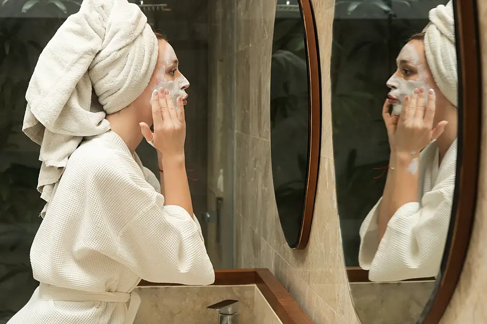 Woman applying beauty face mask in front of the mirror, beauty skin care concept at home