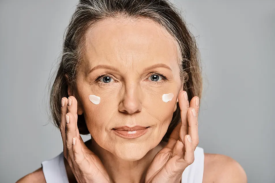 Woman serenely applying cream to her face.