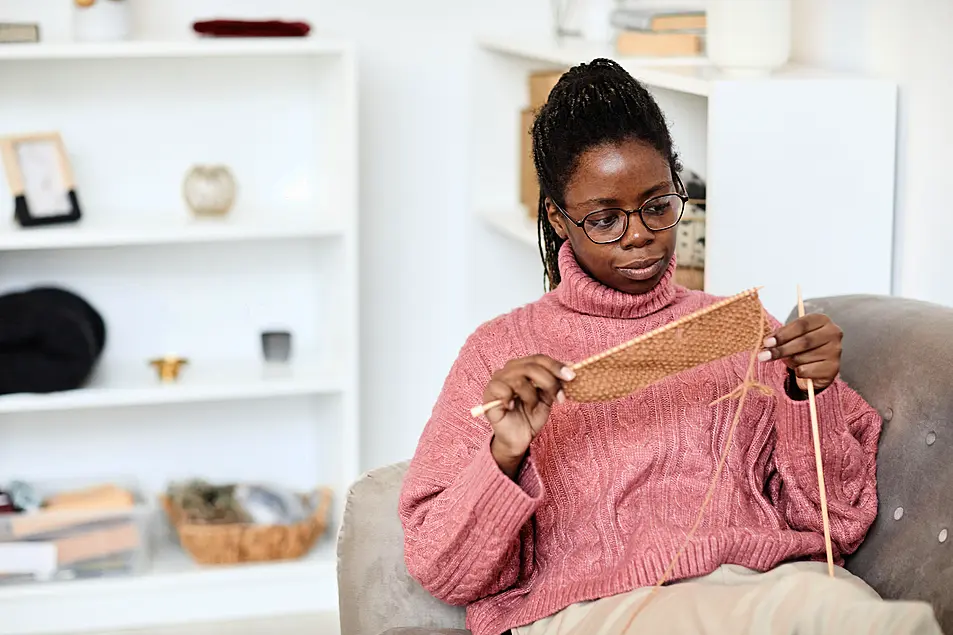 Young woman knitting at home on the sofa