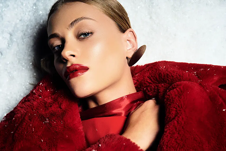 A young woman with bold red lips showcases winter fashion in a snowy landscape.