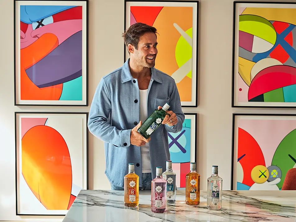 Spencer Matthews holding a bottle of CleanCo gin infront of colourful abstract artwork