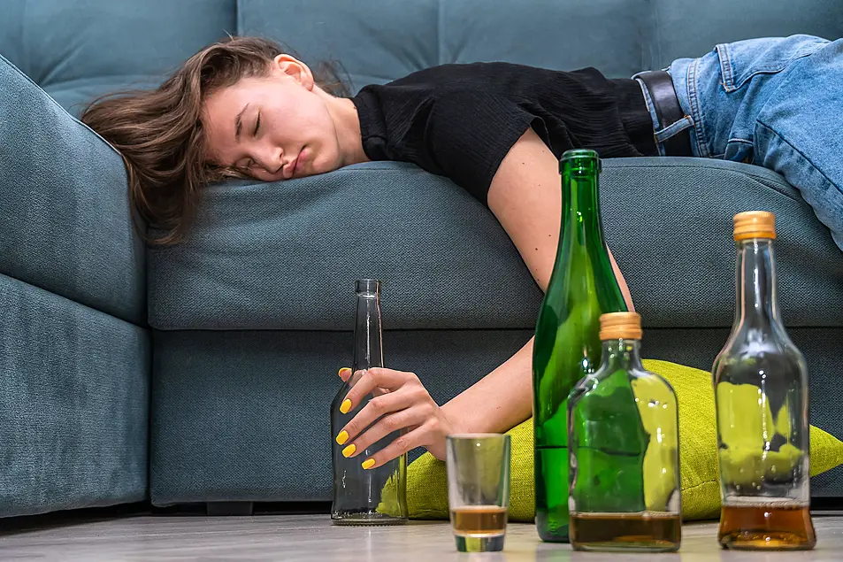  Tired young dark-haired woman lying on the couch after a party at home close-up, next to empty bottles on the floor