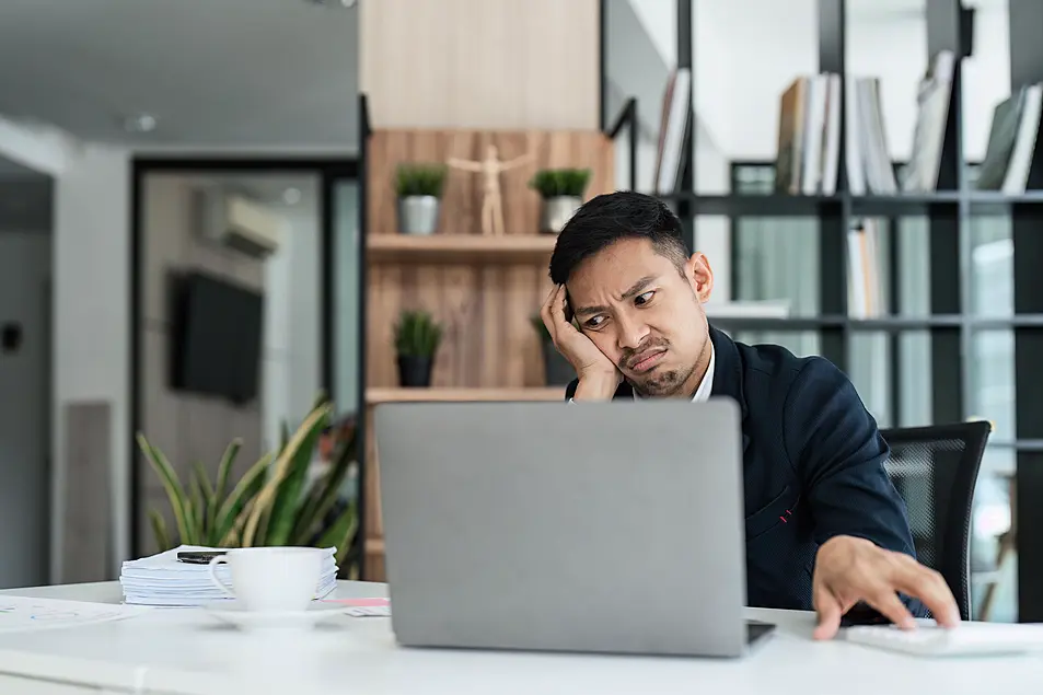 Young man looking at his work laptop feeling tired and stressed