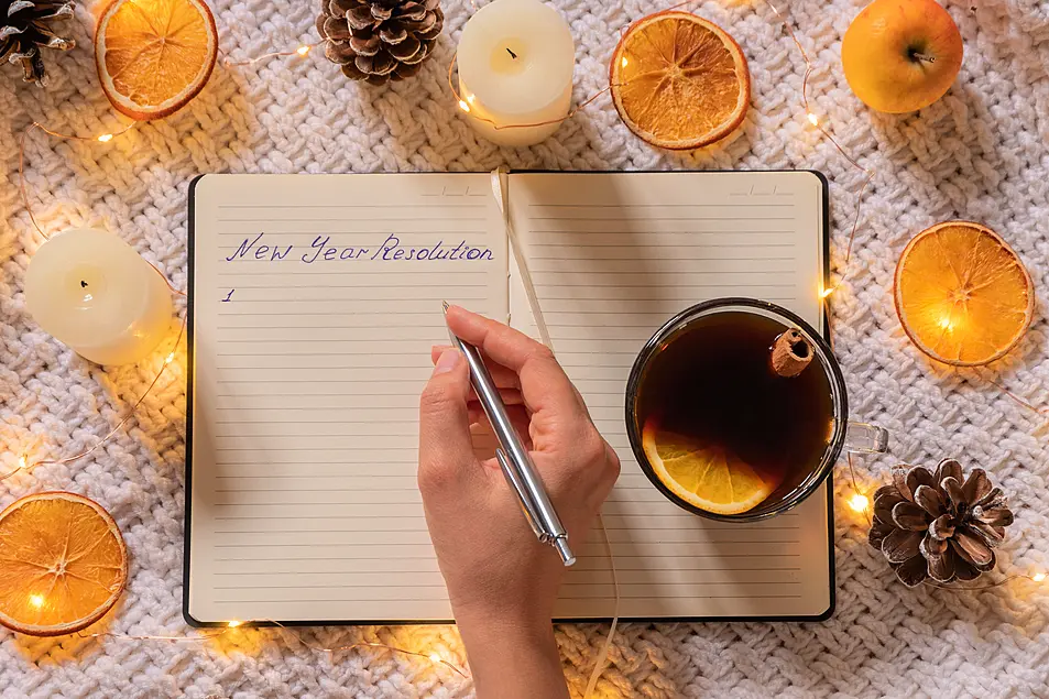 Woman hand holding pen and writing in notebook with black tea and Christmas decorations around her