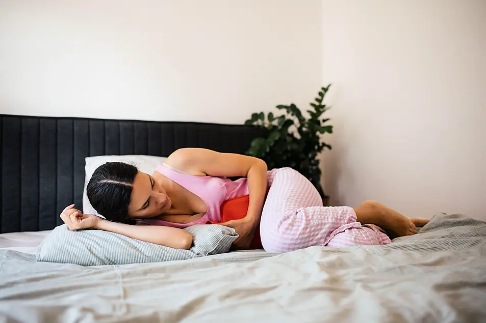 Woman laying in bed with a hot water bottle on her stomach 