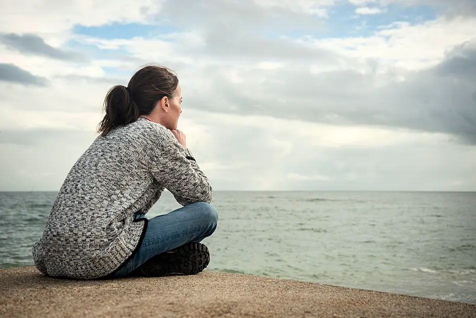 Woman sitting alone looking out to sea deep in thought.