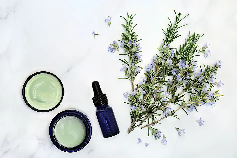 Vegan skin care beauty treatment with rosemary herb flowers, aromatherapy essential oil & moisturiser on marble. Anti ageing benefits.