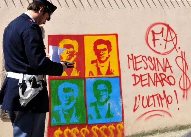 Um policial italiano olha para um grafite no muro perimetral da catedral da cidade de Palermo, retratando Messina Denaro