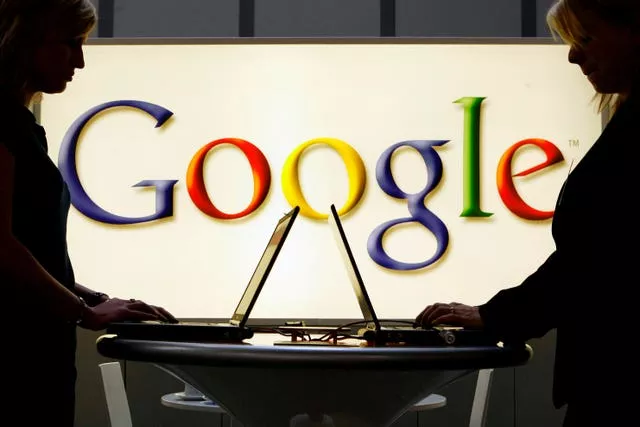 People work on laptops in front of an illuminated sign of the Google logo 