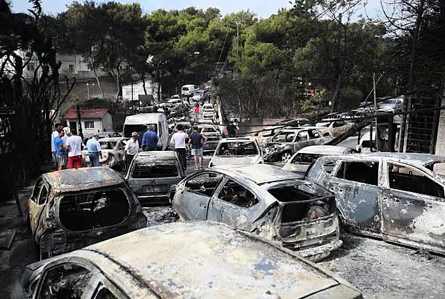 People stand amid the charred remains of burned-out cars in Mati east of Athens, Greece, in July 2018