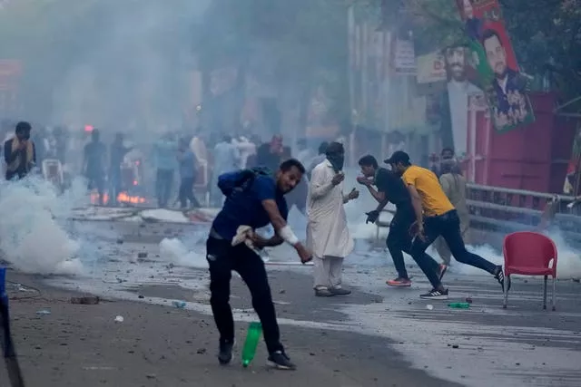 Supporters of former prime minister Imran Khan throw stones as police firing tear gas shells to disperse them during clashes outside Mr Khan’s residence, in Lahore, Pakistan