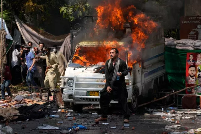 Supporters of former prime minister Imran Khan throw stones toward police next a burning vehicle during clashes in Lahore 