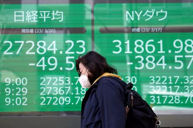 A person walks in front of an electronic stock board showing Japan’s Nikkei 225 and New York Dow indexes at a securities firm on Monday, March 20, 2023, in Tokyo