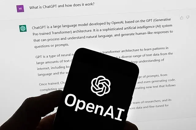 The OpenAI logo on a mobile phone in front of a computer screen which displays output from ChatGPT