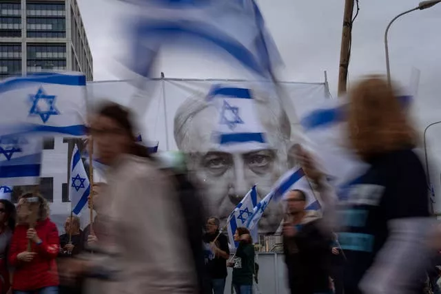 Demonstrators walk with Israel’s national flag next to a banner showing Prime Minister Benjamin Netanyahu during a protest in Tel Aviv against plans by his government to overhaul the judicial system 