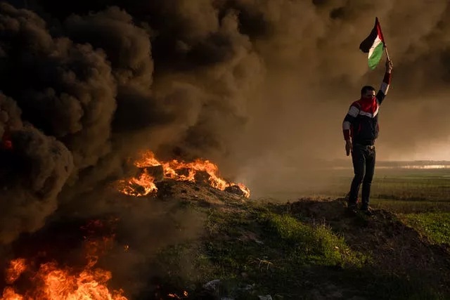 Palestinians burn tyres and wave the national flag during a protest against a Israeli military raid in the West Bank city of Jenin, along the border fence with Israel, east of Gaza City