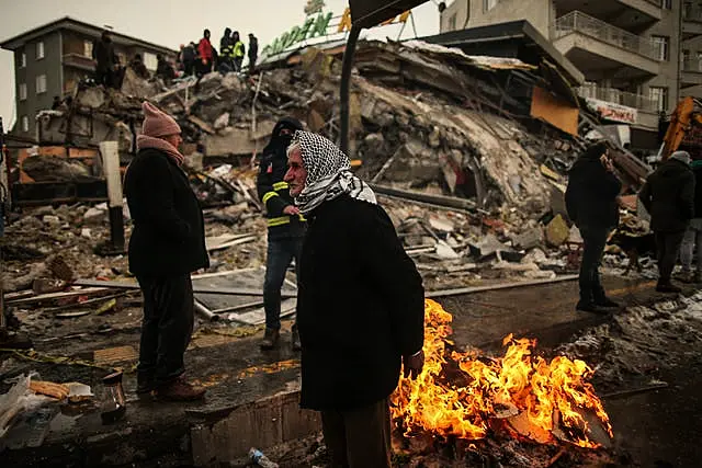 People warm themselves next to a collapsed building in Malatya, Turkey