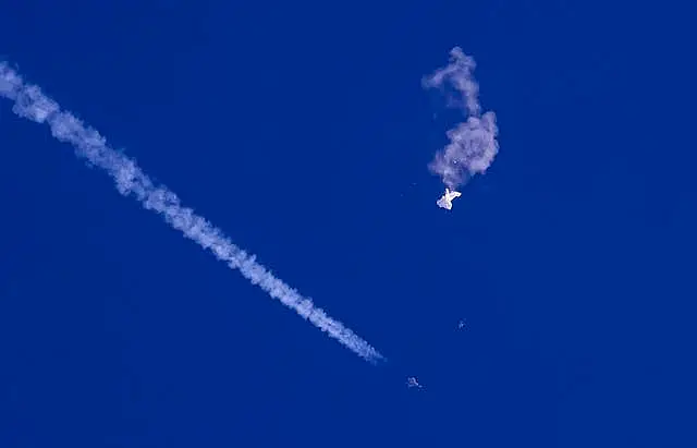 The remnants of a large balloon drift above the Atlantic Ocean, just off the coast of South Carolina, with a fighter jet and its contrail seen below it