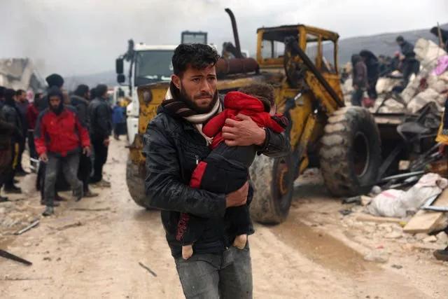 A man carries the body of an earthquake victim in the Besnia village near the Turkish border