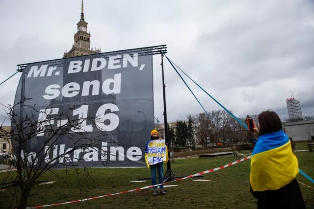 Two protestors wrapped in Ukrainian flags take images next to a sign asking US President Joe Biden to send fighter jets to the Ukraine during the president’s visit to Warsaw