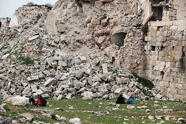 People sit by a building destroyed in recent earthquake in Aleppo, Syria