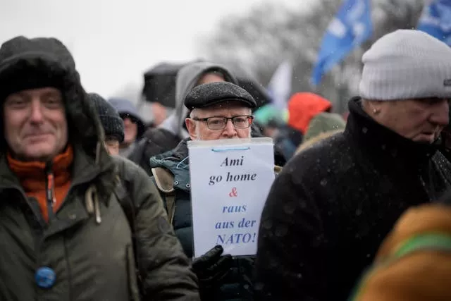 A man holds a poster reading ‘Ami Go Home and Out of the NATO!’