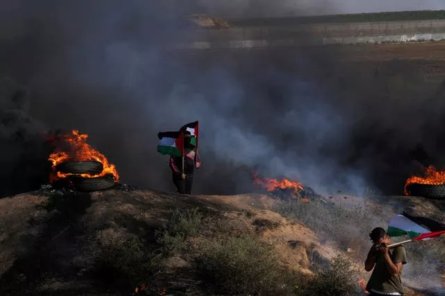 Palestinian demonstrators wave their national flags while others burn tyres during a protest against an Israeli military raid in the West Bank city of Jenin