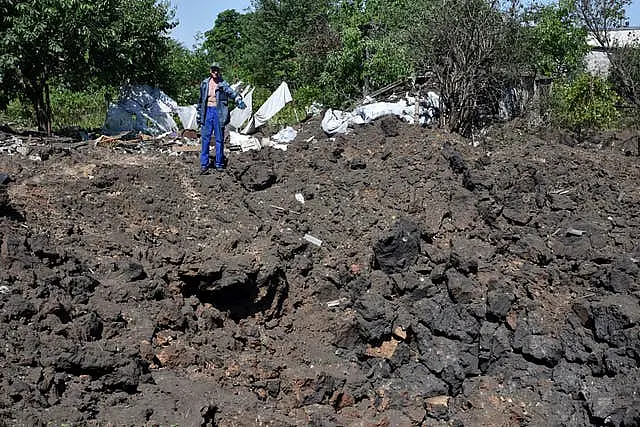 A man gestures next to crater of an explosion by Russian shelling in a residential area in Kushuhum, near Zaporizhia, Ukraine