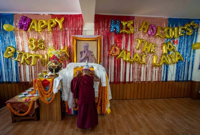 A young monk offers a ceremonial scarf in front of a portrait of his spiritual leader the Dalai Lama