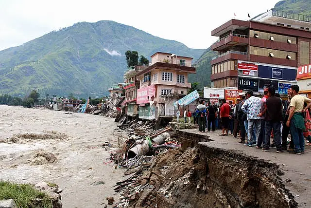 People stand by a road washed away by the River Beas swollen due to heavy rains in Kullu District, Himachal Pradesh, India