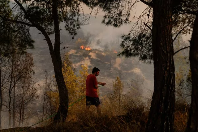 A man tries to extinguish the fire with a hose near Loutraki, 80 kilometres west of Athens