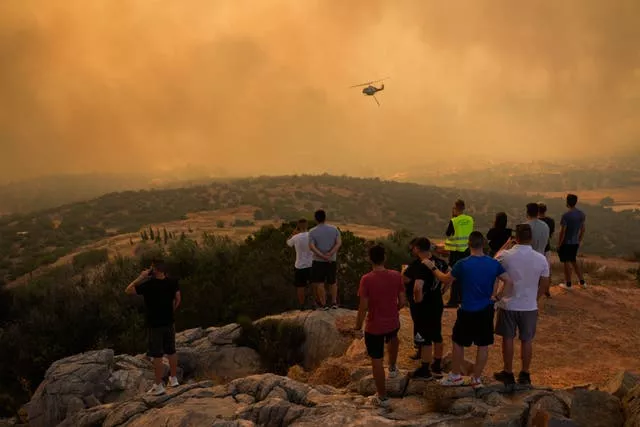 A firefighting helicopter flies through smoke as people look on in Mandra west of Athens