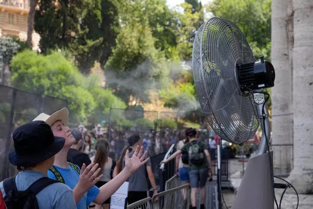 Tourists cool off near a fan as they queue to enter Rome’s Colosseum