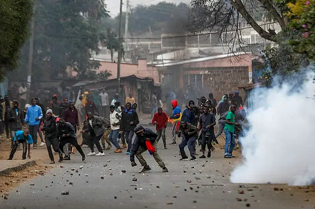 Protesters throw rocks at police during clashes next to a cloud of teargas in the Kibera area of Nairobi