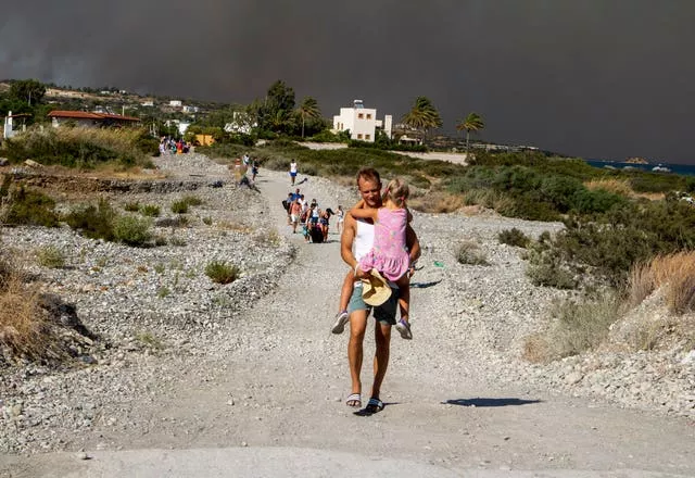 A man carries a child as they leave an area where a forest fire burns on Rhodes
