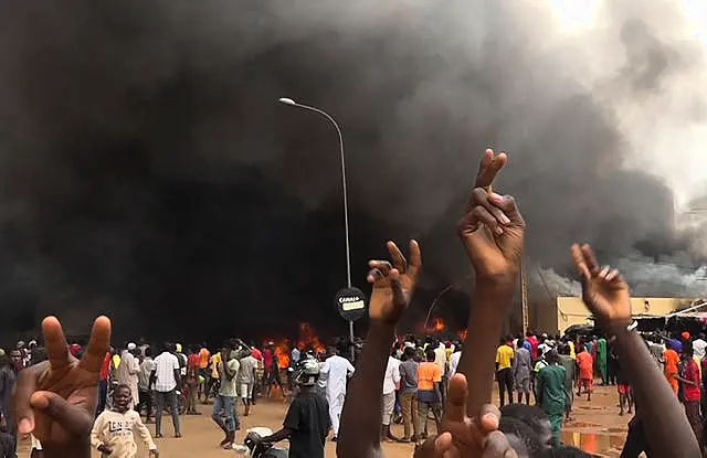 With the headquarters of the ruling party burning in the back, supporters of mutinous soldiers demonstrate in Niamey