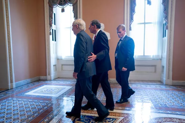 Mitch McConnell, left, is assisted by John Barrasso, second from right, and a Capitol police officer