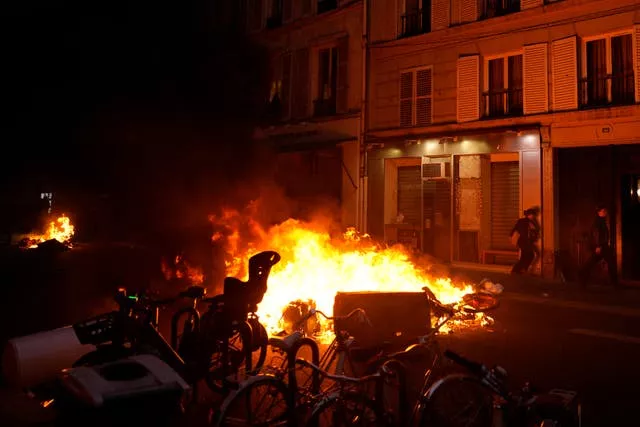 A woman runs past burning rubbish bins and bicycles in Paris after French President Emmanuel Macron tried to defuse tensions in a televised address to the nation