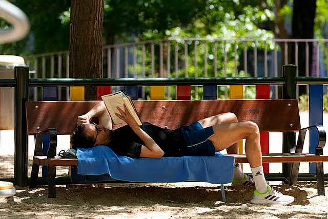 A man lies on a bench in the shade reading a book in Madrid