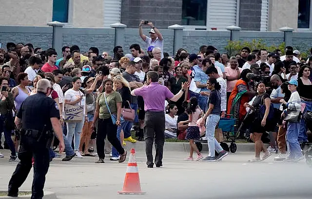 People gather across the street from the shopping centre after a shooting on May 6