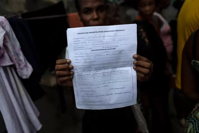 Lovely Benjamin, who was sexually assaulted by a gang member, holds up her medical report in Jean-Kere Almicar’s front yard, where she and her young son have sought refuge, in Port-au-Prince