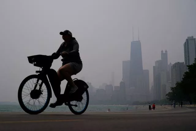 A cyclist rides a bike along the shore of Lake Michigan as the skyline is blanketed in haze