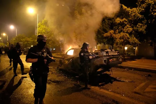 Police officers walk past burned cars as they clash with youths in Nanterre 